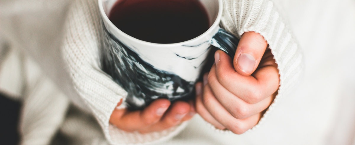 Photograph of a woman's hands holding a cup of tea or coffee in a comforting way.